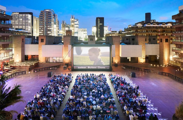 Large crowd watching a film at Barbican Outdoor Cinema, cityscape in the background.