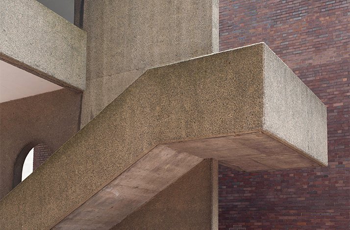 A brutalist concrete staircase structure positioned against a textured brick wall background at The Barbican Centre.