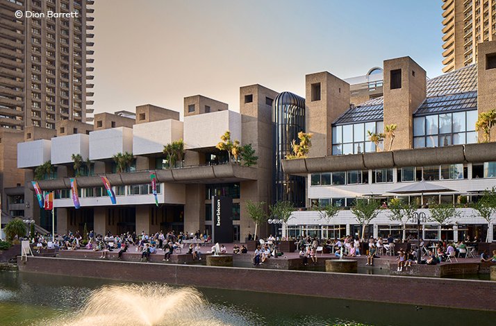 People sitting outside near a waterfront and fountain at London's Barbican Centre.
