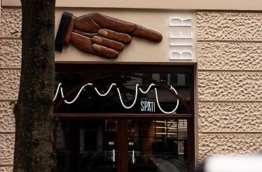 BRLO Charlottenburg exterior in Berlin, with carved wooden pointing hand above neon 'Spati' sign and lit 'Bier' lettering.