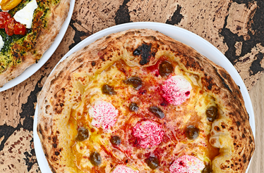 Close-up of a delicious Neapolitan sourdough pizza topped with fresh ingredients, served on a white plate over a cork-textured table.