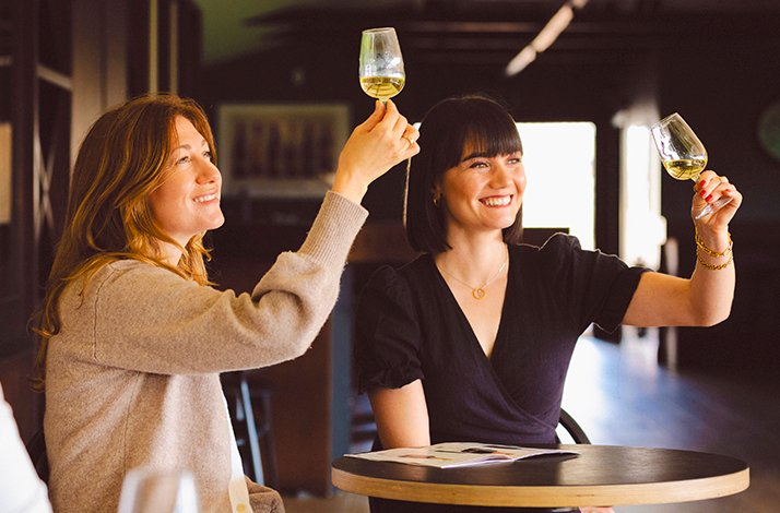 Two people holding up glasses of Chapel Down wine indoors.