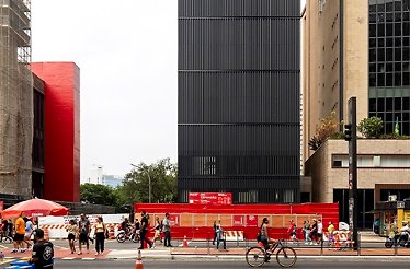 A city street scene in front of the Pietro Maria Bardi building depicts a diverse group of people traversing a crosswalk.