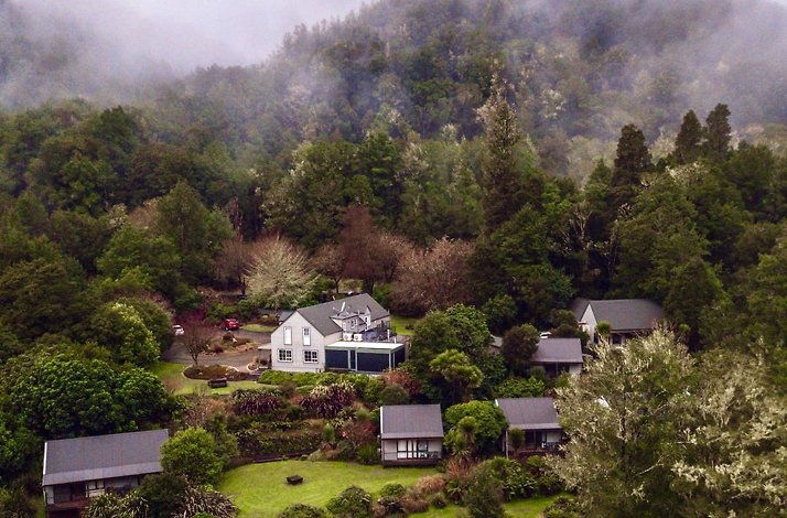 Aerial view of Maruia River Retreat nestled in lush, misty forested hills.