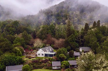 Aerial view of Maruia River Retreat nestled in lush, misty forested hills.
