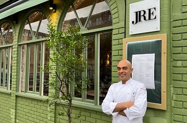 Chef Alfred Prasad standing next to the JRE sign on the facade on restaurant Shiuli
