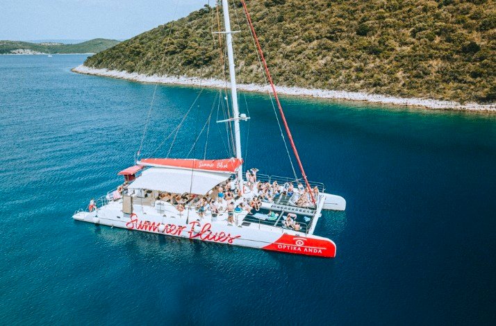 A boat with the Summer blues logo on its board sailing in the costal waters with tourists aboard.