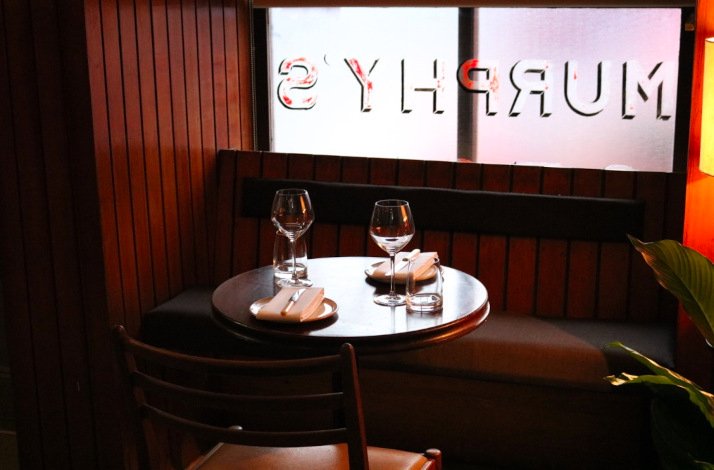 A cozy restaurant table set for two with wine glasses, napkins, and cutlery, beneath a window
