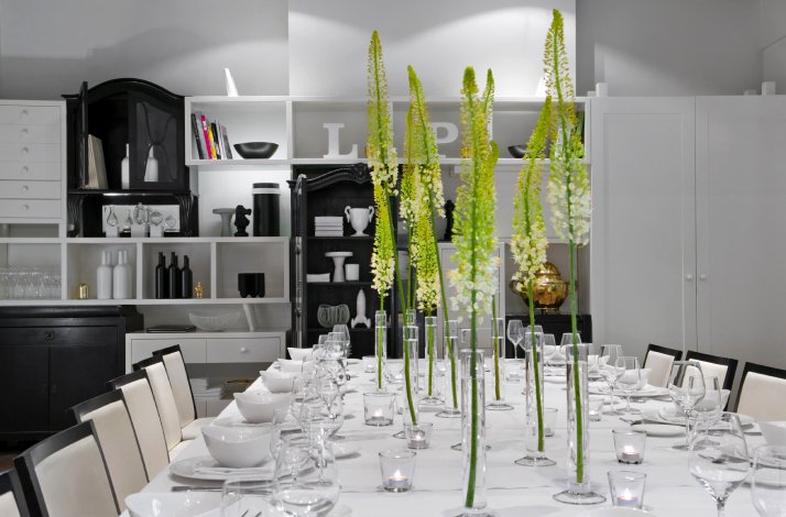 Dubravkin put private dining space featuring a white-set long table, tall green blooms, and black-and-white cabinetry.