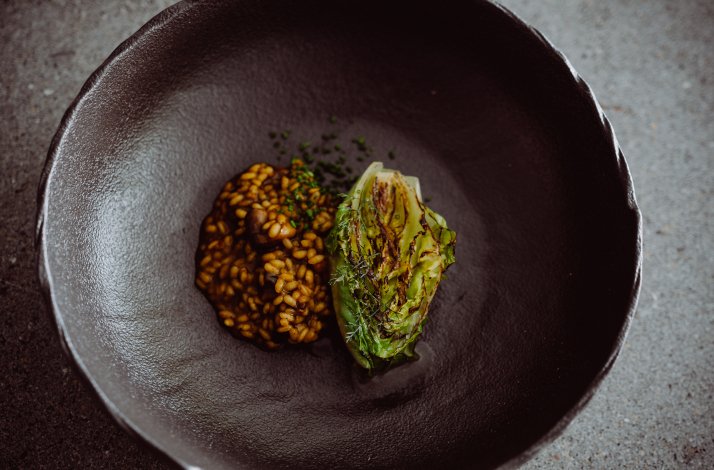 A special dish with smoked cabbage and grains served in a black bowl from the special six course menu at Muxgo restaurant.