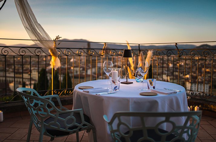 Rooftop terrace table set for two at La Leggenda dei Frati, with Florence's cityscape glowing under a dusk sky.