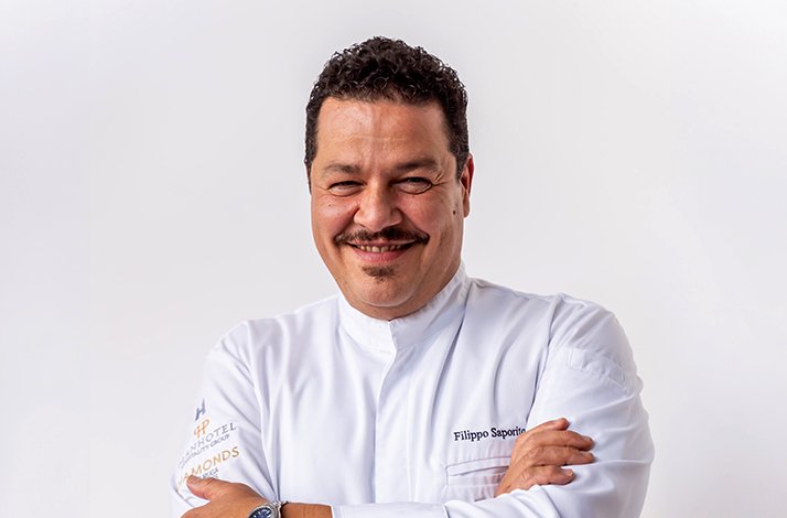 Chef Filippo Saporito smiling with arms crossed, wearing a white chef's jacket with Hotel Diamonds logo.