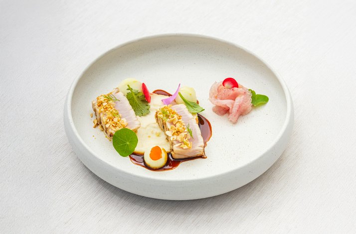 Fine-dining fish dish topped with crushed nuts, edible flowers, and quail egg on white ceramic plate at La Leggenda dei Frati.