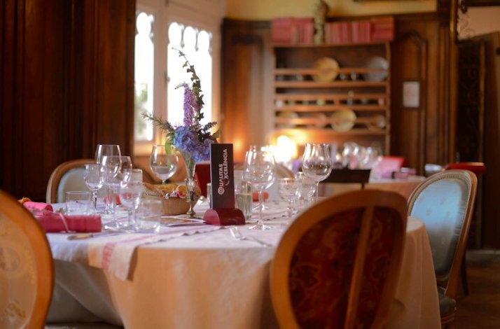 A beautifully set table in a formal dining room with chairs around the table, with white tablecloths, napkins and a vase of flowers at Restaurant G.a.