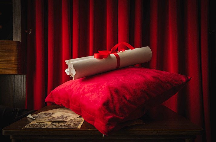 A rolled parchment tied resting on a red pillow used during the cabaret-style live performances