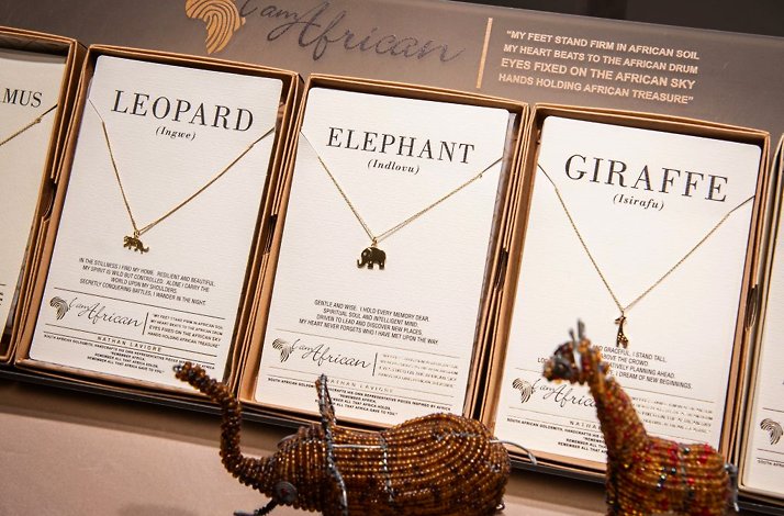 'I Am African' branded gold necklaces with Leopard, Elephant, and Giraffe pendants displayed in boxes with beaded figurines.