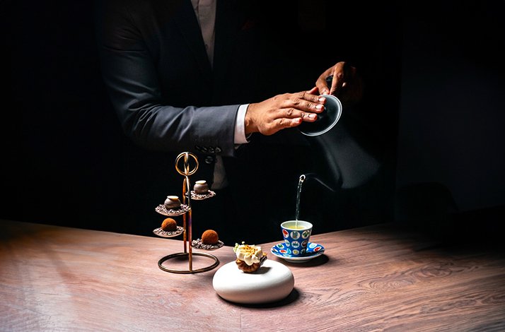 A waiter serving water to a cup, a table full of desserts 