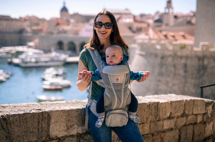 A person holding their child in a sling and posing on a bridge in Dubrovnik