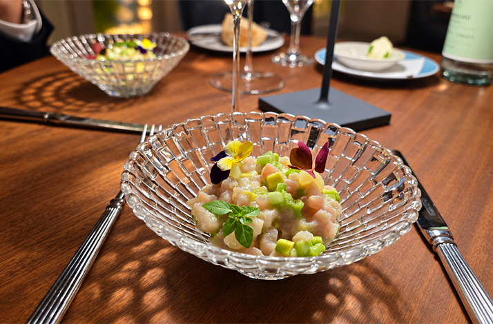 Seafood tartare with avocado and edible flowers in a glass bowl on a set table at Atlantik Fisch.