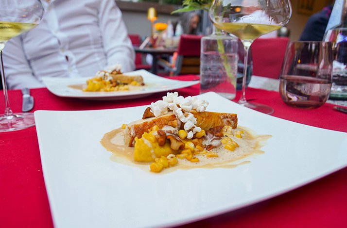Golden seared course topped with mushrooms, corn, and popcorn served at a Huber Munich dinner table with wine pairing.