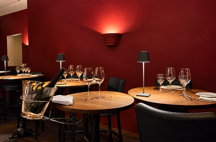 Cozy dining room at Atlantik Fisch with round wooden tables, wine glasses, and warm red walls.