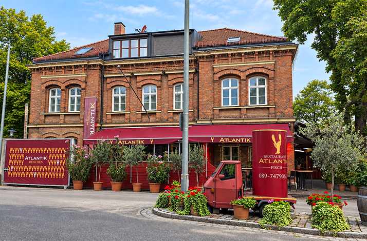 Exterior of Atlantik Fisch restaurant with red awnings, potted plants, and branded delivery van.