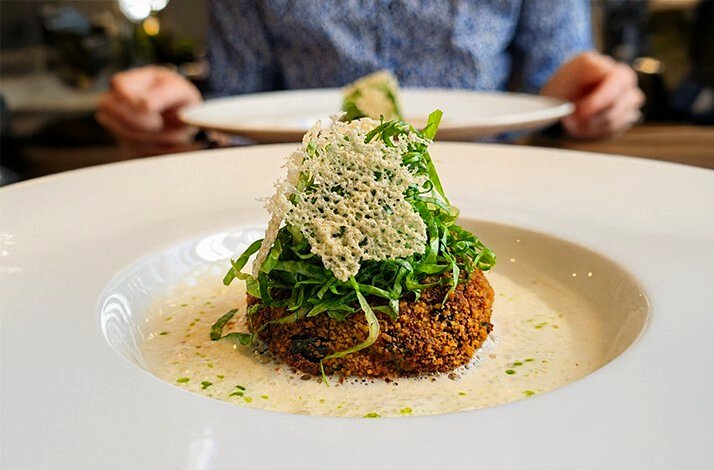 Delicate dumplings with golden breadcrumb topping in pale cream sauce on a white plate, paired with white wine at a Munich curated tasting dinner.