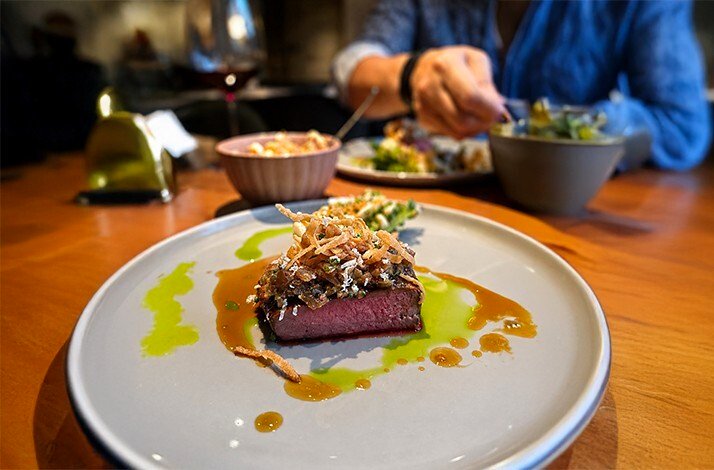 Seared meat medallion topped with herb crust and crispy onion straws, finished with herb oil and jus, part of a curated Munich off-menu tasting course.