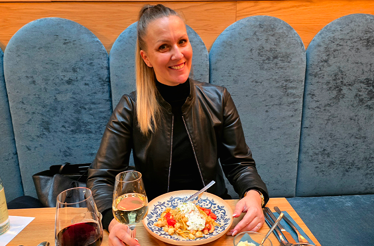 Bianca Murthy smiling with a glass of wine and a plate of pasta.