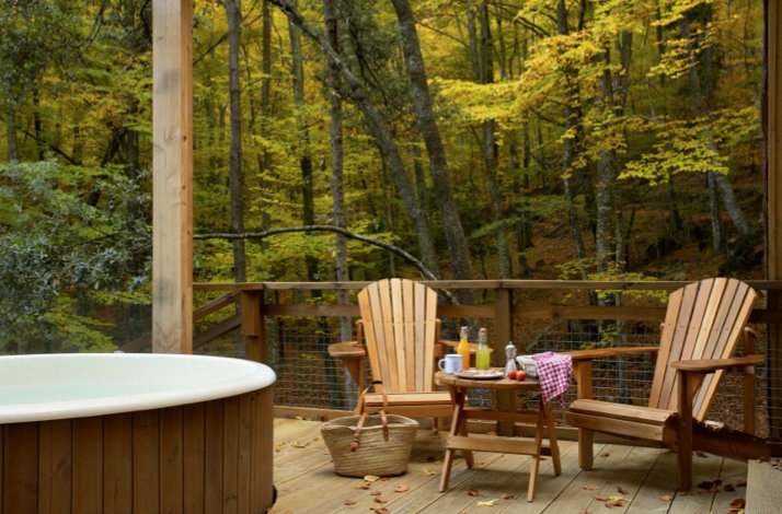 Secluded cabin terrace featuring a hot tub, lounge chairs, and a breakfast tray set against a forest backdrop. Confidence: High