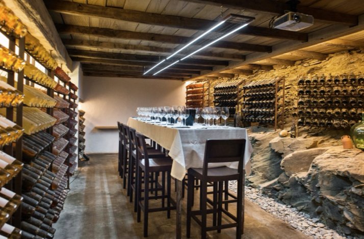 A wine cellar with stone wall and wooden tables for wine tasting experience at Hotel Cala Jóncols