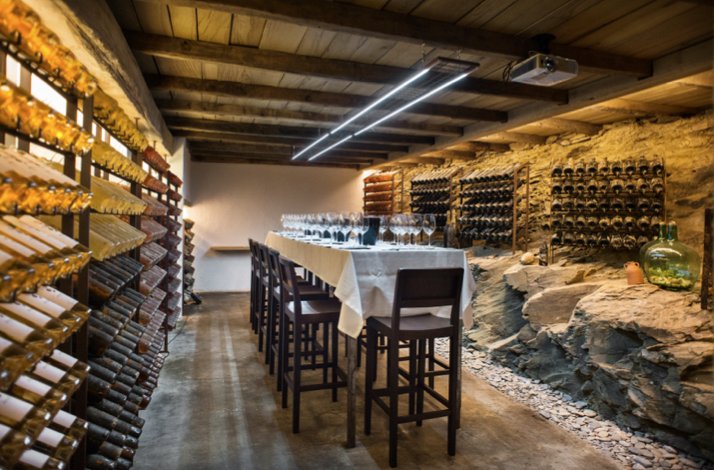 Wine cellar at Hotel Restaurante Cala Joncols, featuring floor-to-ceiling bottle racks and a set long table with wine glasses.