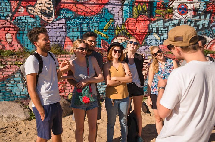 A group of young people smiling and posing in front of a wall with street art.