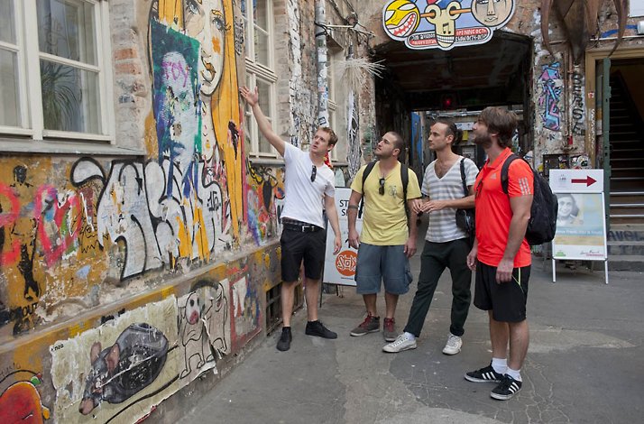 A guide explaining street art to three men.