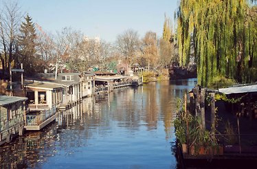 View of a river with a willow tree and small fishing houses along the shore.