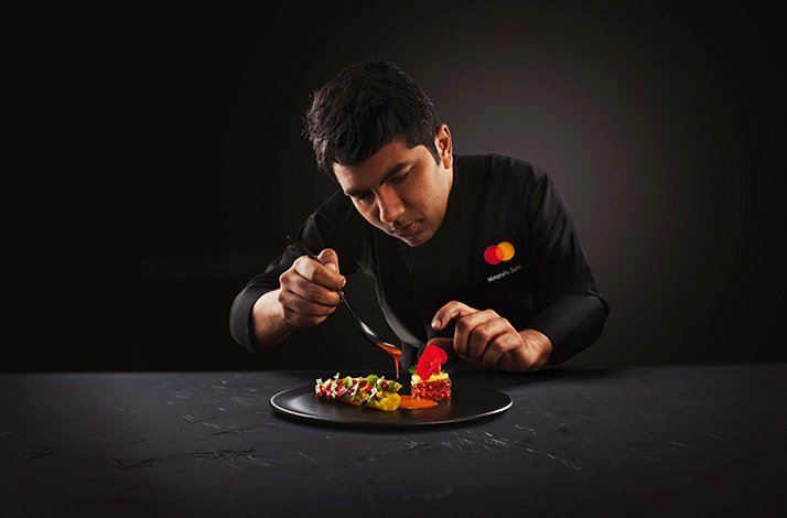 The chef wearing the uniform with the branded MC logo in the process of preparing the dish. has context menu