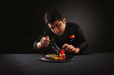 The chef wearing the uniform with the branded MC logo in the process of preparing the dish. has context menu