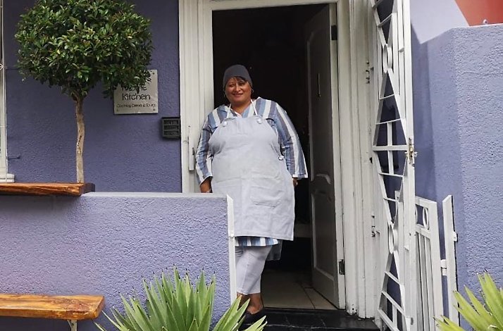 Lady wearing white apron near purple house, Cape Town, South Africa.