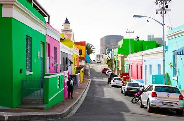 A street in Cape Town with brightly colored buildings on both sides, including green, pink, yellow, and blue.