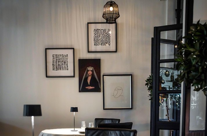 Elegant restaurant dining room in Rura with white-clothed tables, black leather chairs, table lamps, and framed art on the wall.
