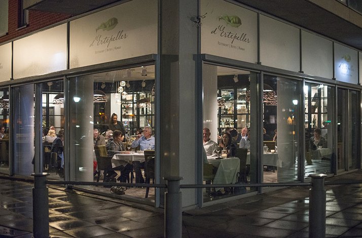  An outdoor dining area of a De Ertepeller restaurant at night, with guests.