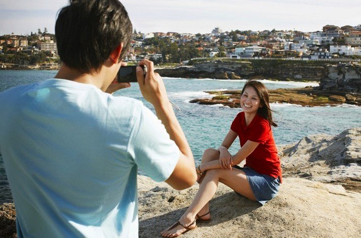 A man captures a photograph of a woman at the Bondi beach.