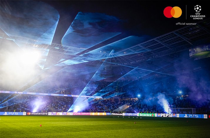 A stadium highlighted by a dynamic blue laser and light show before an UEFA Champions League match. Mastercard and UEFA Champions League logos at the top right corner.
