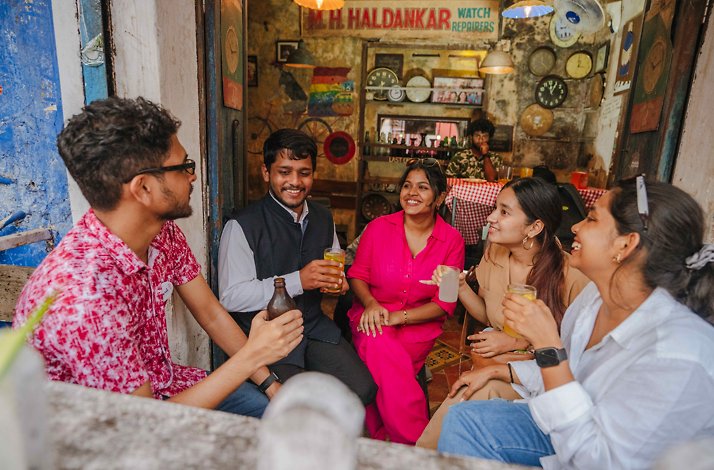 Five tourists sitting and chatting, enjoying drinks at a restaurant in Panaji, India.