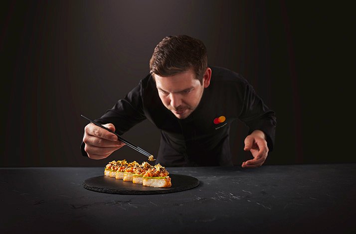 The chef wearing the uniform with the branded MC logo in the process of preparing the dish. has context menu