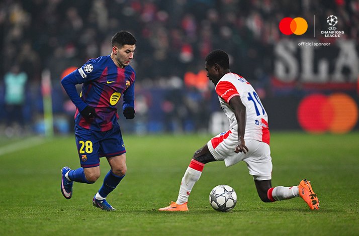 FC Barcelona's number 28 driving past SK Slavia Praha's number 18 during a UEFA Champions League 2025/26 league phase match, Upper-right corner: Mastercard logo + UEFA Champions League logo with text 'official sponsor'
