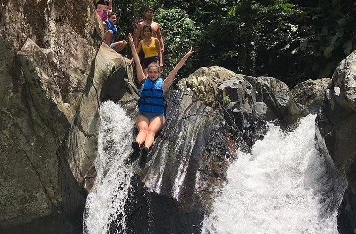 A group of people sliding down a rock waterslide at Puerto Rico's famed El Yunque rainforest.