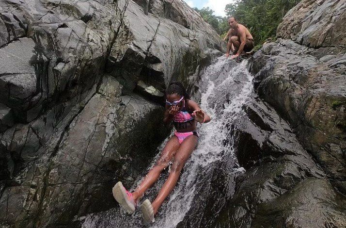 A couple sliding down a rock waterslide at Puerto Rico's famed El Yunque rainforest.