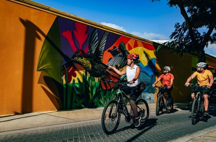 Three cyclists pass by the amazing street art at Oranjestad, Aruba.