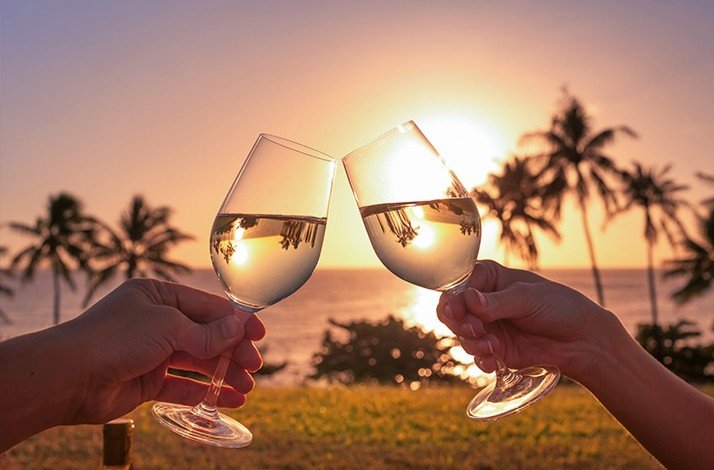 Two people toast with wine glasses on the Barbados beach.
